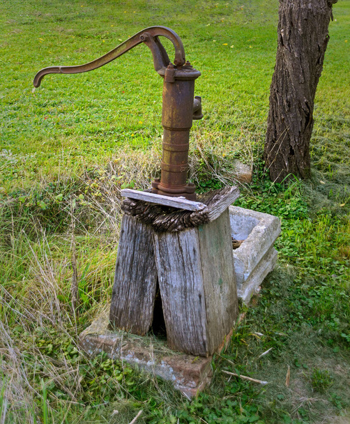 старый ржавый ручной насос на гнилом деревянном основании, расположенном на лугу, Австрия - Фото, изображение