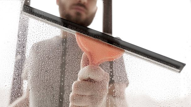 Samiec myje okna w domu. Sprzątanie domu. Pranie brudnych szklanych detergentów do mycia okien. Czyszczenie szklanki za pomocą wycieraczki, zbliżenie. - Zdjęcie, obraz
