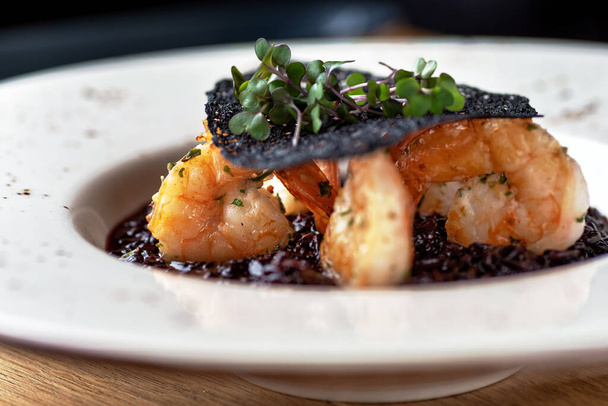 Schwarzreis-Risotto. Shrimp Risotto auf einem weißen Teller auf dem Tisch, serviert in einem Restaurant, Menü Food-Konzept. - Foto, Bild