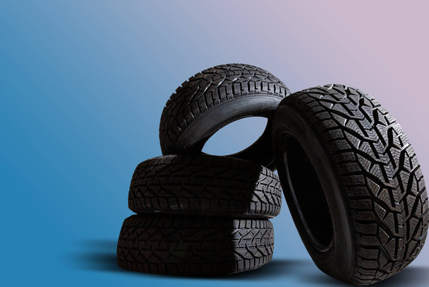 Empilement de quatre nouveaux pneus noirs pour voiture d'hiver sur fond bleu - Photo, image