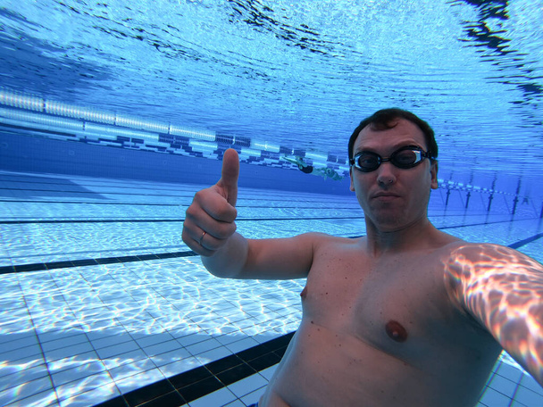 uimari veden alla uima-altaassa osoittaa peukalot ylös - Valokuva, kuva