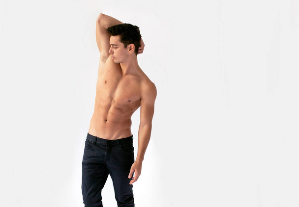 Sexy young man with nacked torso in black jeans, posing in studio with his hand raised, isolated on a white background. - Фото, зображення