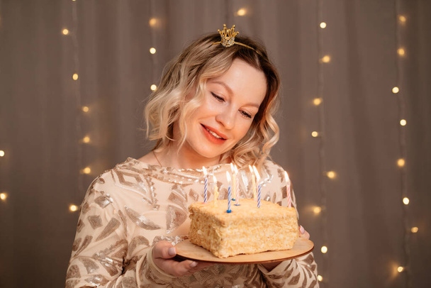 Beautiful blonde woman in small crown on head with a birthday cake and candles. - Фото, зображення