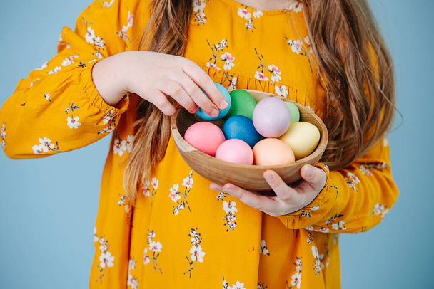 Little girl holding plate with easter eggs over blue - Foto, Imagem