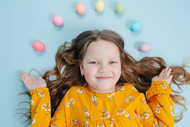 Happy little girl lies on a floor with a rainbow of easter eggs over her head - Foto, Imagem