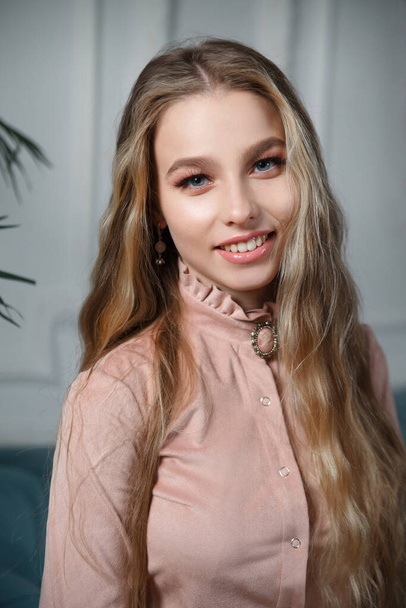 Beautiful blonde girl with long hair in a delicate vintage look in a powdery pink dress in the interior. - Valokuva, kuva