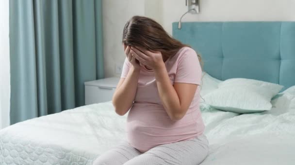 Üzgün, ağlayan, depresyonda olan hamile bir kadın yatakta oturuyor ve başını tutuyor. Annelik ve hamilelik depresyonu kavramı. - Video, Çekim