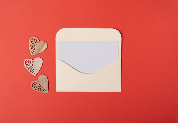 Envelope with a blank sheet of paper inside and wooden hearts on the red background. Romantic love letter for the Valentine's day concept. Space for text. - Foto, immagini