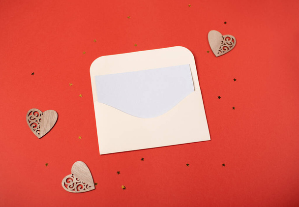 Envelop met een blanco vel papier binnenkant en houten hartjes op de rode achtergrond. Romantische liefdesbrief voor het Valentijnsdag concept. Ruimte voor tekst. - Foto, afbeelding