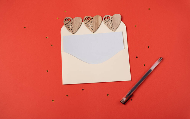 Envelope with a blank sheet of paper inside and wooden hearts on the red background. Romantic love letter for the Valentine's day concept. Space for text. - Foto, Bild