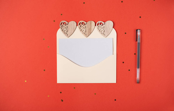 Envelope with a blank sheet of paper inside and wooden hearts on the red background. Romantic love letter for the Valentine's day concept. Space for text. - Photo, Image