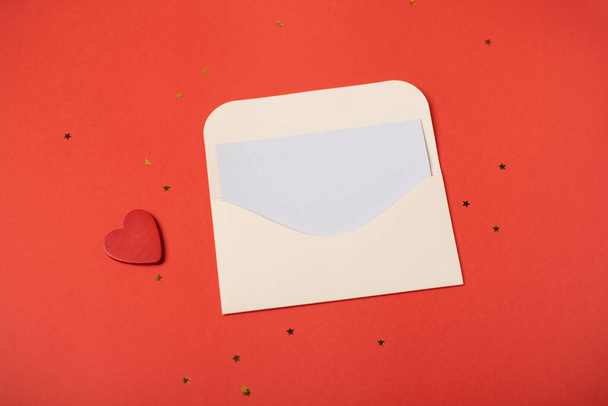 An envelope with a red wooden heart on it on the red background. Flat lay, top view, space for text. Romantic love letter for Valentine's day concept. - Photo, Image