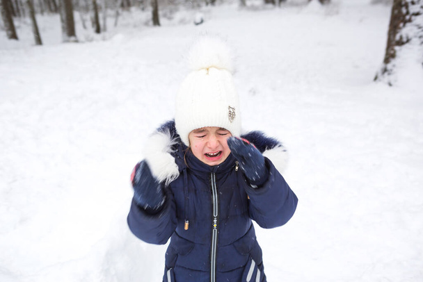 Little girl crying outside in winter. A child in warm clothes is upset, cold, wipes away tears, screams, is capricious and hysterical. Winter, snow, frost, children's hysteria, discontent - Photo, image
