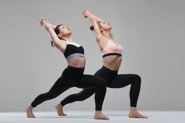 Two girl practicing yoga isolated on gray background. - Foto, afbeelding