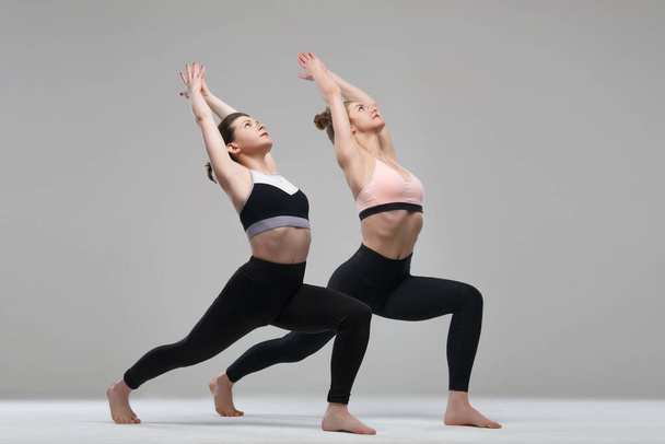 Two girl practicing yoga isolated on gray background. - Zdjęcie, obraz