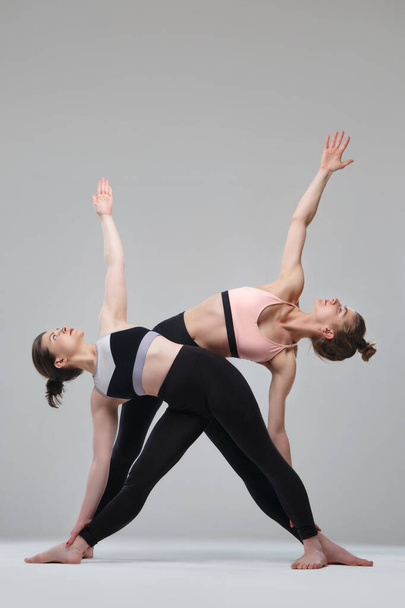 Two girl practicing yoga isolated on gray background. - Фото, зображення