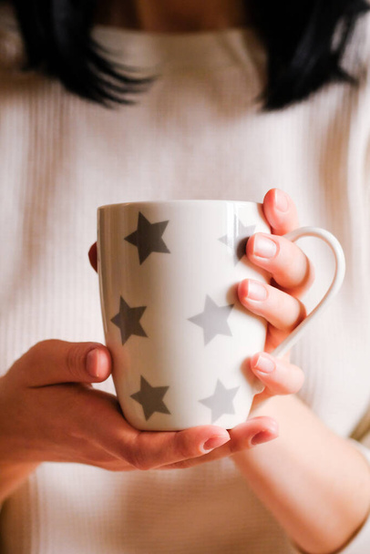 A menina com as roupas aconchegantes segurando uma xícara de café. Mãos femininas com bebida quente, no fundo claro - Foto, Imagem