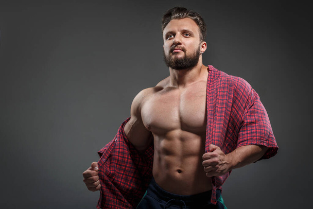 Muscular sexy white man takes off shirt isolated on dark background. - Fotó, kép