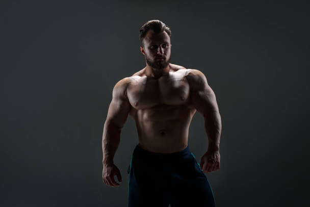 Courageous athletic guy with a naked torso in the backlight against a dark background. - 写真・画像