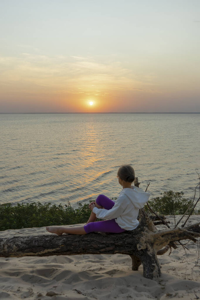 Κορίτσι χαλαρώνει στο ηλιοβασίλεμα πάνω από τη θάλασσα - Φωτογραφία, εικόνα
