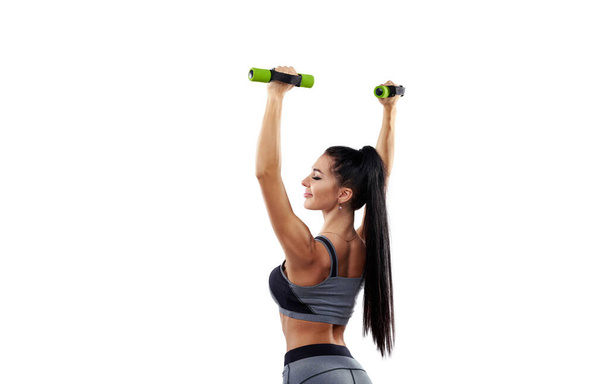 Vista das costas para uma mulher fitness segurando halteres e levantando as mãos isoladas no fundo branco. - Foto, Imagem