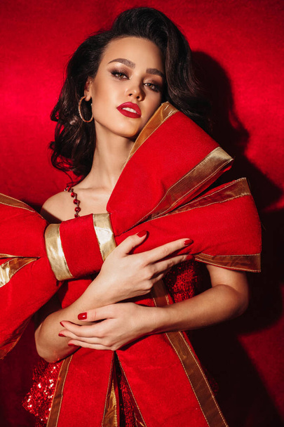 fashion holiday photo of  beautiful brunette woman wearing a big gift red bow ad a dress, posing in studio - Fotoğraf, Görsel