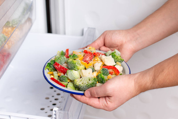冷凍野菜:ブロッコリー、トウモロコシ、エンドウ豆、カリフラワー、ピーマン、冷蔵庫の冷凍庫でプレート上の緑豆. - 写真・画像