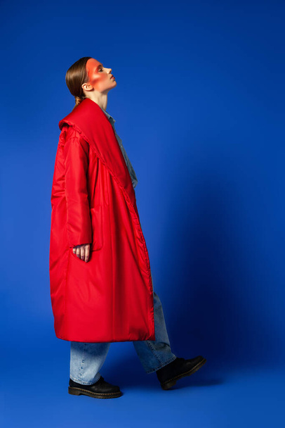 Female model in baggy coat walking against blue background - Foto, Bild