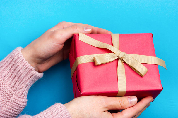 Female hands hold a pink gift tied with a beige ribbon. The moment of giving a gift. - Foto, imagen