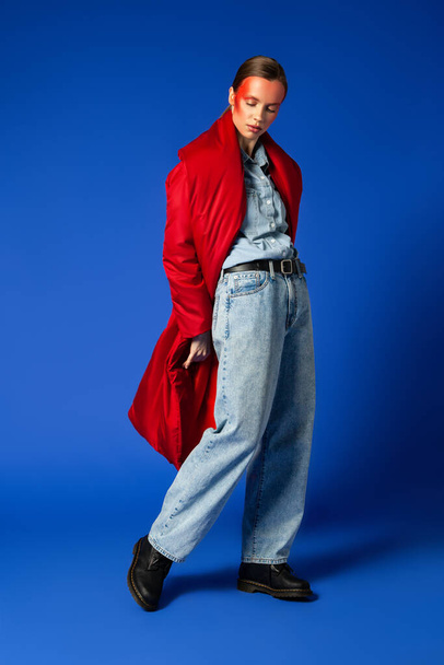 Female model in baggy coat walking against blue background - Zdjęcie, obraz