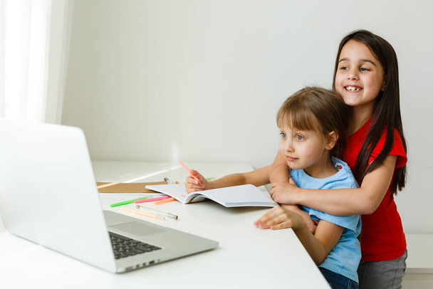 Kaksi tyttöä, vanhin ja nuorin, ovat mukana pöydässä kannettavalla tietokoneella. - Valokuva, kuva