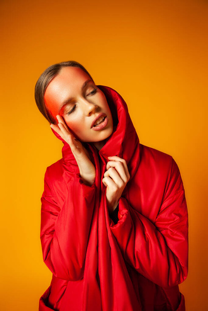 Woman in trendy coat touching face against yellow background - Φωτογραφία, εικόνα