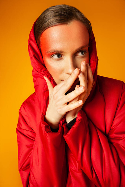 Woman in trendy coat touching face against yellow background - Foto, imagen
