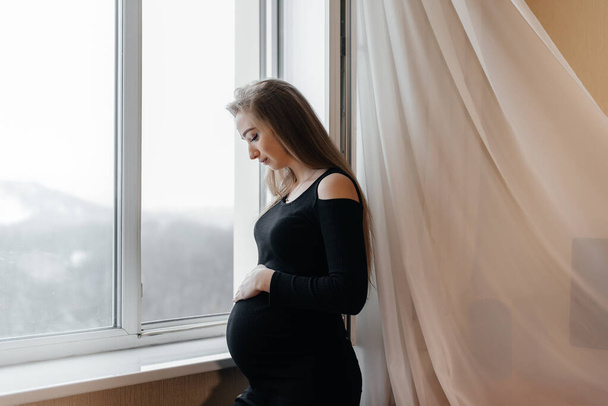 A pregnant girl is breathing fresh air from the window - Fotó, kép