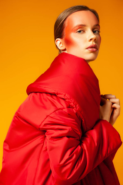 Young woman wrapping in red coat against yellow background - Foto, Imagem