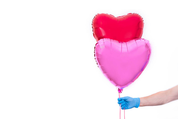 Courier in protective gloves holds red heart-shaped balloon for Valentine's Day. Safe contactless home delivery of gifts to your favorite women on Mother's and Women's Day.I love you. Hand close up - Zdjęcie, obraz