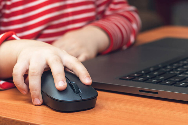 Child's hand holds a computer mouse, child learns and plays on the computer. - Photo, image