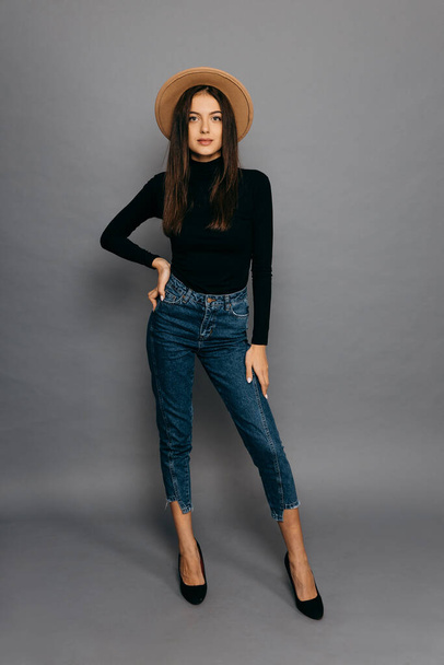 Beautiful girl in black body suit, jean and straw hat, isolated on grey background - Foto, imagen
