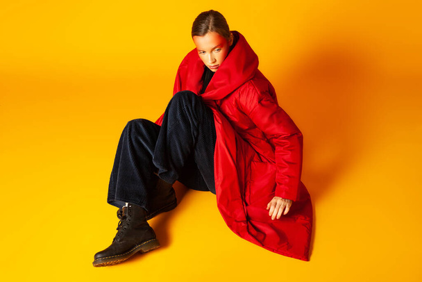 Lonely woman wrapping in baggy coat against yellow background - Фото, зображення