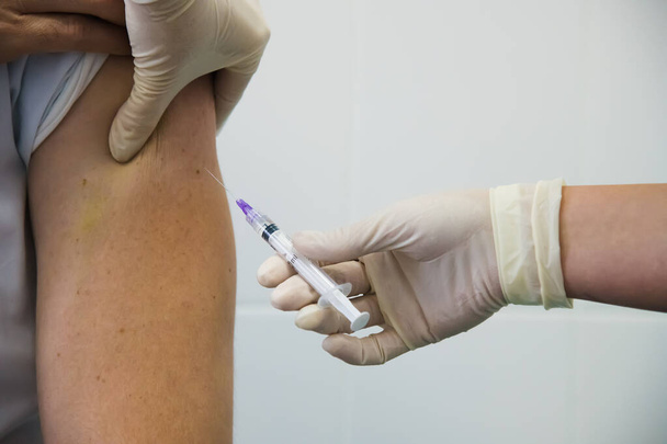 Εμβολιασμός κατά του κορωνοϊού. Μαζικός εμβολιασμός. Ο γιατρός εγχέει το εμβόλιο γρίπης, πνευμονίας ή COVID-19 στον ώμο του ασθενούς - Φωτογραφία, εικόνα