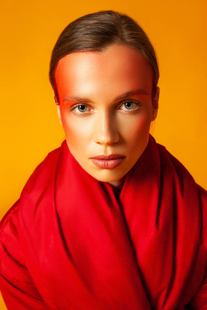 Young woman wrapping in red coat against yellow background - 写真・画像