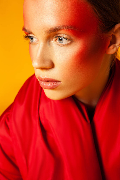 Young woman wrapping in red coat against yellow background - Fotografie, Obrázek