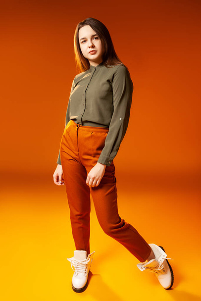 Trendy young woman looking at camera against orange background - Foto, imagen