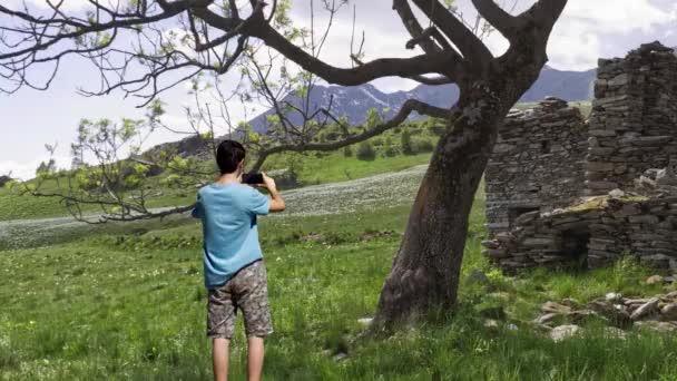 krajobraz paralaksy chłopca stojącego na bocznicy patrzącego na kamienną chatkę zanurzoną między górami. cynemagraf - Materiał filmowy, wideo