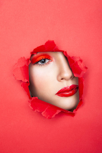 Woman with red visage looking through torn paper - Fotó, kép