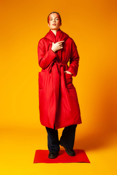Female model in trendy red coat against yellow background - Foto, afbeelding