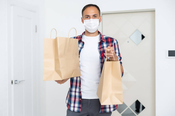 Courier σε προστατευτική μάσκα παραδίδει takeaway τροφίμων. Υπηρεσία παράδοσης υπό καραντίνα, εστία νόσου, coronavirus covid-19 πανδημία συνθήκες. - Φωτογραφία, εικόνα