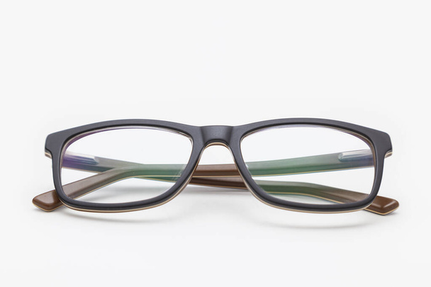 Eine dunkel umrandete Brille von vorne betrachtet, mit den Schläfen gekreuzt und auf einer weißen Oberfläche platziert. Der Hintergrund ist weiß. Sideburns werden durch die Linse gesehen. - Foto, Bild