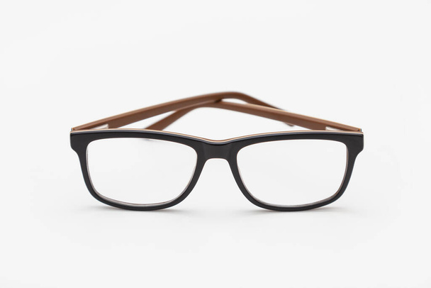 Un par de gafas de borde oscuro vistas desde el frente, con las sienes cruzadas y colocadas sobre una superficie blanca. El fondo es blanco. - Foto, imagen
