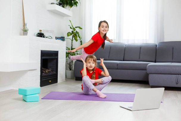 deux petites filles pratiquant le yoga, étirement, remise en forme par vidéo sur ordinateur portable. Formation en ligne à distance, aérobie à la maison. Mode de vie sain, coronavirus, restez à la maison. Enfant sport maison quarantaine. - Photo, image